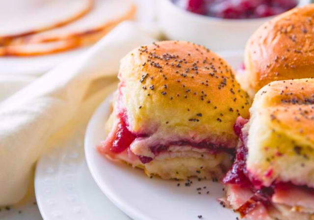 Golden turkey cranberry sliders with melted cheese and cranberry sauce on a festive holiday platter.