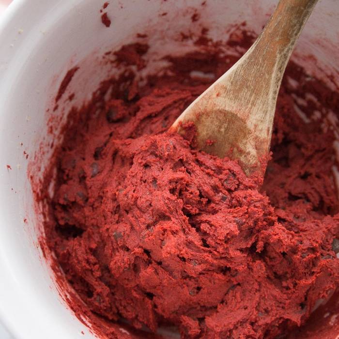 I have a love affair with anything red velvet, and this red velvet cookie recipe is a must make this Valentine's Day. It is topped with a Hugs Hershey's Kiss. #cookies #valentinesday #redvelvet #easy #recipe #best #withhersheykiss #gooey #tasty red velvet cookie dough in a bowl with spoon