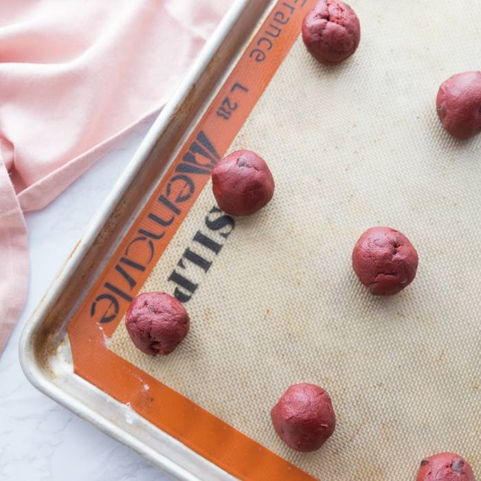 I have a love affair with anything red velvet, and this red velvet cookie recipe is a must make this Valentine's Day. It is topped with a Hugs Hershey's Kiss. #cookies #valentinesday #redvelvet #easy #recipe #best #withhersheykiss #gooey #tasty red velvet cookie dough on baking sheet