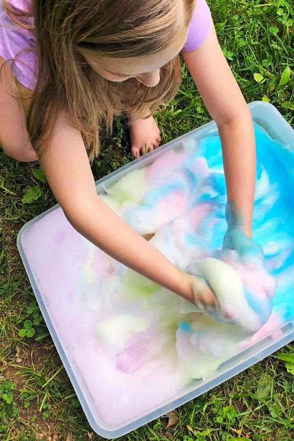 Tie Dye Soap Foam is a must-make for kid activities. All you need is a little soap and food coloring to make this sensory play activity. #passion4savings #tiedye #soap #foam #colorful #outdoor #activity #sensoryplay #fun #forkids playing with soap foam in back yard