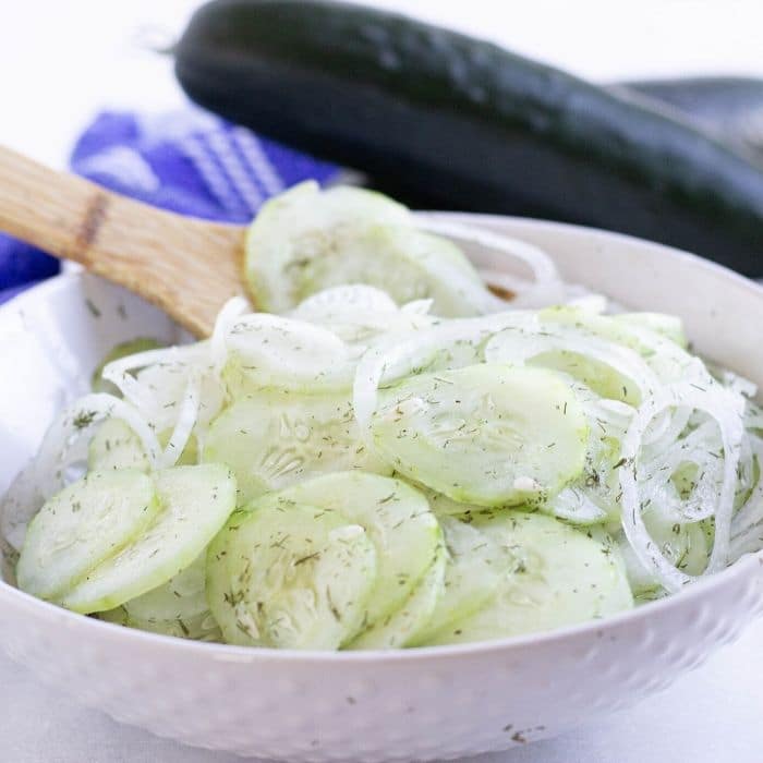 cucumber and onions in a white bowl with wooden spoon in it 
