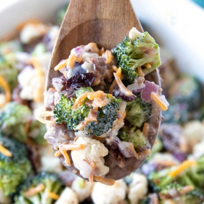 Broccoli Cauliflower Salad is the ultimate side dish or potluck dish. Broccoli, cauliflower, cranberries all mixed in a creamy and sweet sauce. #broccoli #cauliflower #easy #sidedish #holiday #Potluck #passion4savings #creamysauce #Homemade #fresh #vegetables broccoli salad on wooden spoon