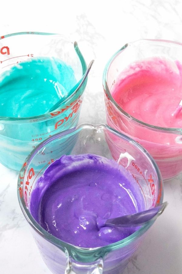cake batter colored all different colors in measuring cups 
