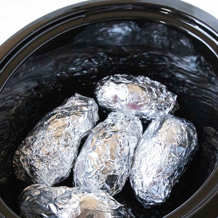 baked potatoes wrapped in aluminum foil on slow cooker 