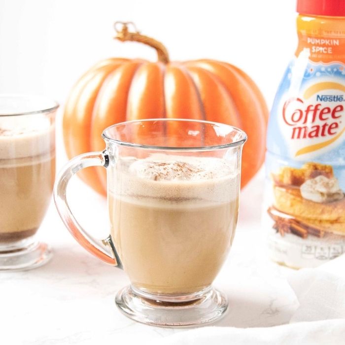 pumpkin spice latte with creamer behind it 