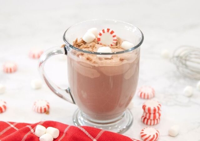 cup of peppermint whipped hot chocolate with candies around it