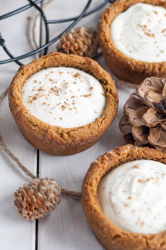 eggnog cheesecake cookie cups on table with pinecones around it 