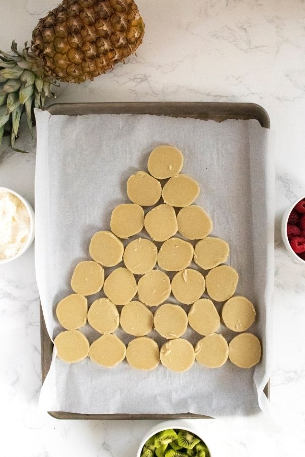 Christmas Tree Fruit Pizza is a simple dessert that is a tree shaped dessert. Whip this up for serving friends and family this season. #christmas #passion4savings #best #easy #sugarcookie #cheesecake #fruit #kidfriendly #easyrecipe #dessert sugar cookie cookies shaped as a tree on parchment lined paper