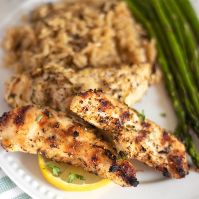 grilled lemon pepper chicken on a plate with lemon slice, rice and vegetables 