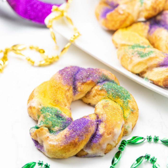 Easy Kings Cake Recipe that uses cinnamon rolls as the base. Quick, easy and just 5 minutes of prep before these cakes are in the oven! #passion4savings #madigras #cake #kingcake #cinnamonroll #dessert #breakfast #kidfriendly cinnamon roll king cake on counter with beads around it