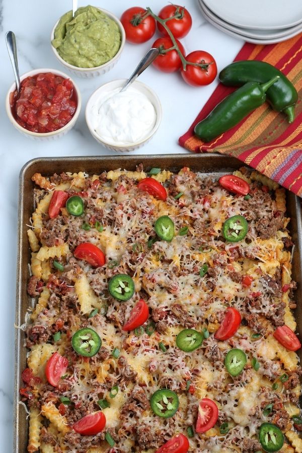 loaded nacho fries on counter with ingredients around it 