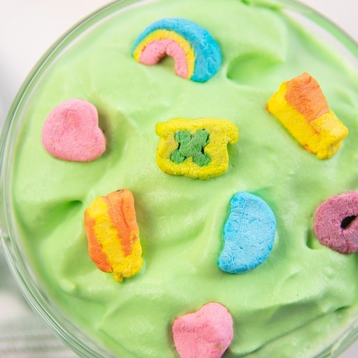 Whipped Shamrock Hot Chocolate is a minty whipped hot chocolate perfect for St. Patrick's Day. A kid friendly mint cocoa recipe that is fun. #passion4savings #shamrock #hotchocolate #tiktok #stpatricksday #stpattyday #kidfriendly #5minute #green #cocoa overhead close up of a whipped green hot chocolate with lucky charm marshmallows on top