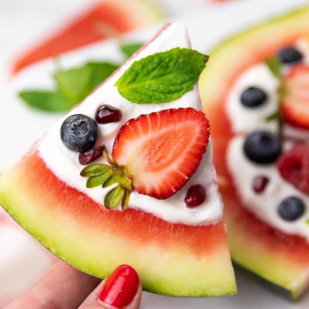 Serve up this delicious watermelon pizza that is topped with yogurt, fresh fruit, and is refreshing. A fun summer dessert idea. #watermelon #dessert #idea #recipe #best #homemade #summer #watermelonpizza #dessertpizza #fruit dessert pizza being held