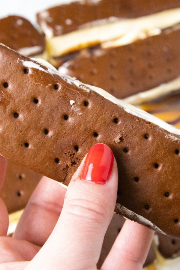 4th of July Ice Cream Sandwich Cake is an easy no bake summer dessert made with ice cream sandwiches. A simple 4th of July dessert! #4thofjuly #passion4savings #easy #nobake #dessert #summer #memorialday #patriotic #5minute #layeredtreat holding ice cream sandwich in hand