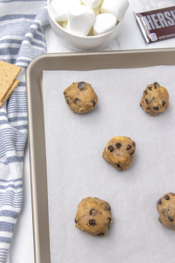 S'mores stuffed cookies are a loaded chocolate chip cookie. Loaded with graham cracker, chocolate and marshmallows in each bite! Give these cookies a try soon! #passion4savings #cookies #smores #stuffed #chocolatechip #marshmallows #grahamcracker stuffed cookies on cookie sheet