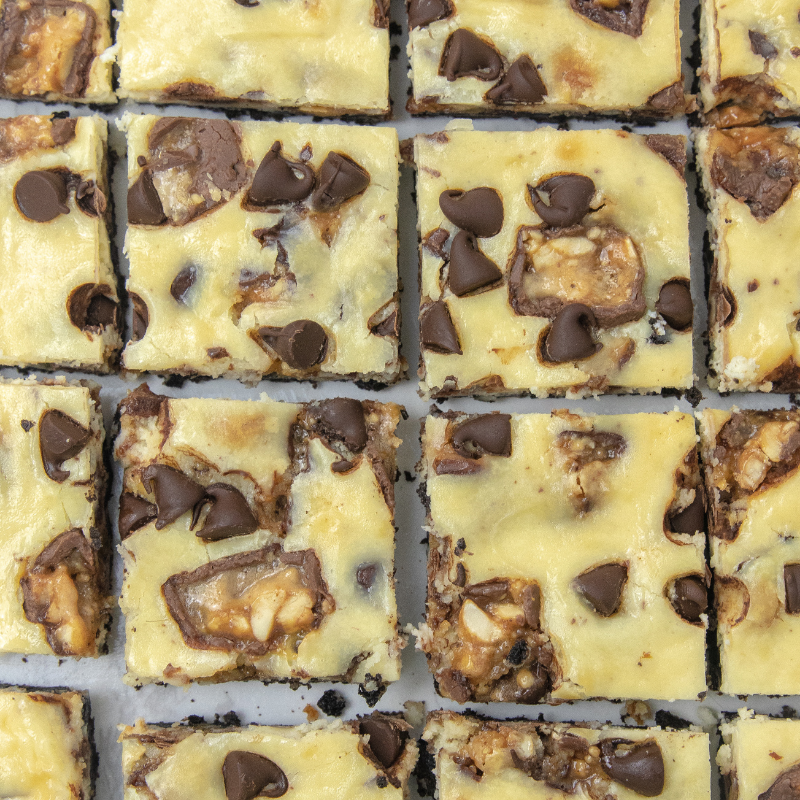Oreo Snickers Cheesecake Bars are an easy and delicious creamy cheesecake with an Oreo cookie crust. A must make baked cheesecake recipe. #passion4savings #snickers #cheesecake #oreo #crust #dessert #best #homemade #simple #summer cut up cheesecake bars on table