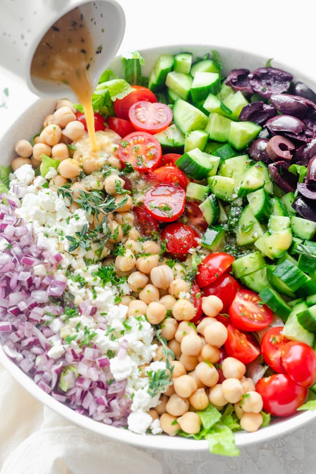 Mediterranean chopped salad with rows of veggies, chicken pea, and dressing being poured on