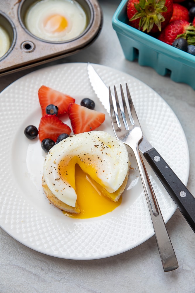 oven poached egg on plate with fork and knife and berries 
