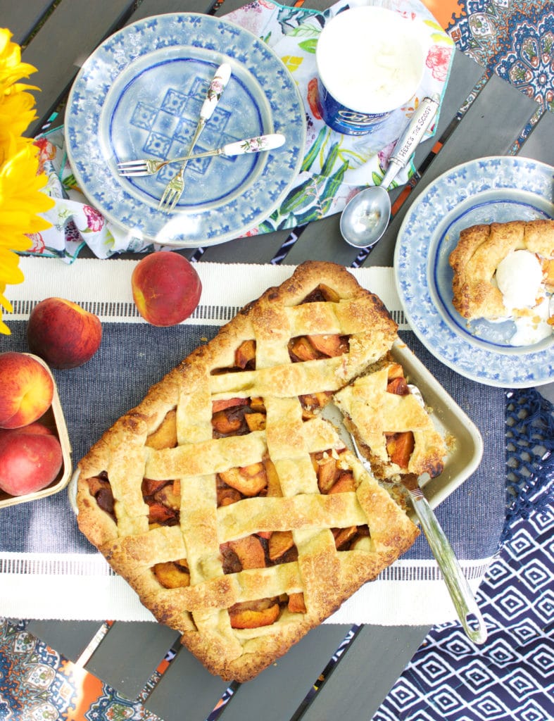 slab peach pie on table with peacnes and plates around it