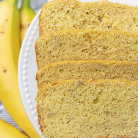 sliced banana bread on a plate iwth bananas by it