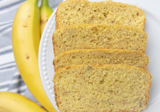 sliced banana bread on a plate iwth bananas by it