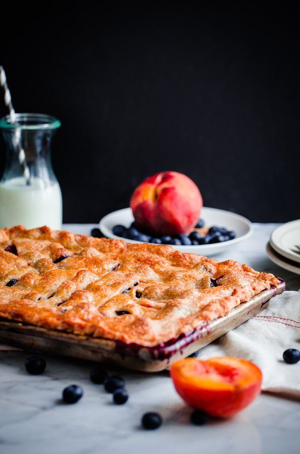 sheet pan pie with blueberries and peaches in a bowl behind it 