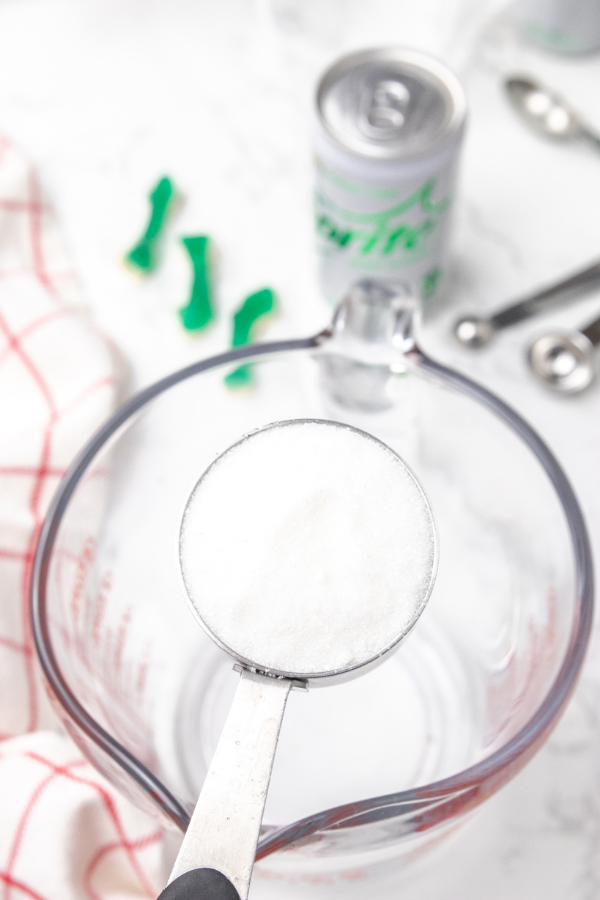 Serve up this delicious and easy shark week ocean water drink. A blue coconut ocean water that is topped with shark gummies! A must make! #passion4savings #shark #sharkweek #drink #oceanwater #drinkrecipe #bluecoconut #bluedrink #kidfriendly #familyfriendly pouring sugar in water