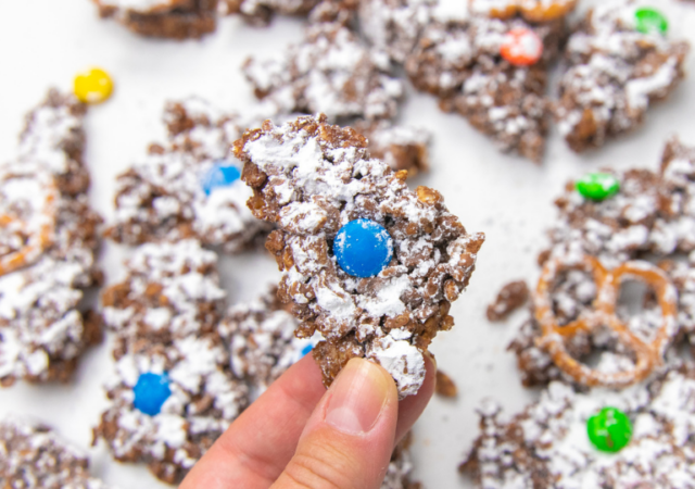 holding a poece of chocolate muddy buddies bark in hand