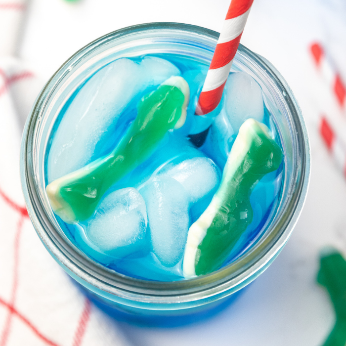 Serve up this delicious and easy shark week ocean water drink. A blue coconut ocean water that is topped with shark gummies! A must make! #passion4savings #shark #sharkweek #drink #oceanwater #drinkrecipe #bluecoconut #bluedrink #kidfriendly #familyfriendly overhead shot of shark drink with shark gummies in it