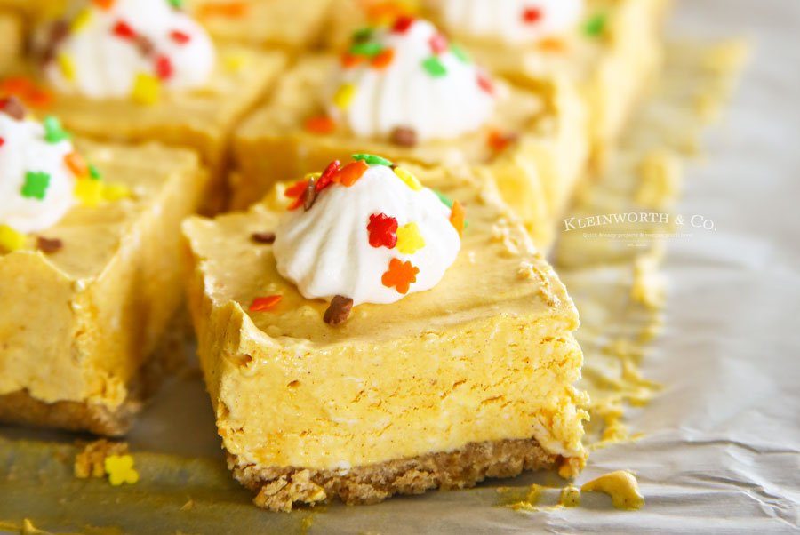 sliced pumpkin cheesecake bars with whipped cream and sprinkles on top 