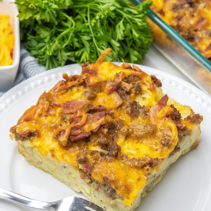 Breakfast Casserole with Hashbrowns is the perfect way to kickstart your day. Bacon, sausage, hashbrowns, all baked in one cheesy casserole. Make ahead breakfast casserole for holidays, or meal prepping breakfast! #passion4savings #breakfast #casserole #hashbrowns #bacon #sausage #cheesy #recipe #fromscratch slice of breakfast casserole on plate with fork by it