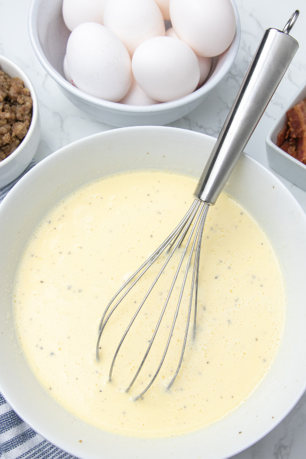 Breakfast Casserole with Hashbrowns is the perfect way to kickstart your day. Bacon, sausage, hashbrowns, all baked in one cheesy casserole. Make ahead breakfast casserole for holidays, or meal prepping breakfast! #passion4savings #breakfast #casserole #hashbrowns #bacon #sausage #cheesy #recipe #fromscratch eggs whisked in bowl on table