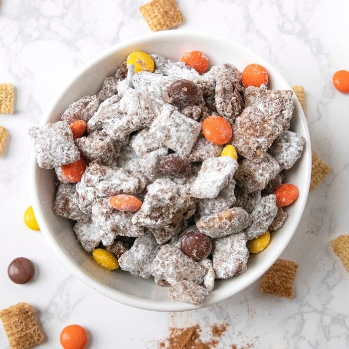 pumpkin spice puppy chow in a bowl with candies around the bowl