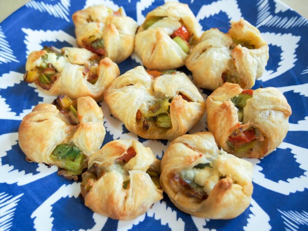 Puff Pastry Appetizers are a fun and easy appetizer that is a perfect finger food for your next party. This puff pastry recipe list is so good. #puffpastry #passion4savings #appetizer #snack #snackidea #partyfood #fingerfood #simple #delicious #fun puff pastry with leeks and cheese on a blue plate
