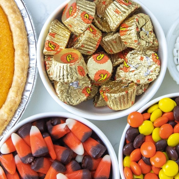 Mini Pumpkin Pie Turkeys are a simple and easy Thanksgiving dessert that are adorable. A round pumpkin pie topped with candies to look like a turkey. A fun and cute Thanksgiving treat for kids and adults. #passion4savings #dessert #thanksgiving #easy #fun #kid #holiday #simple #treatrecipe items for fall on counter - candy corn, Reeses, pumpkin pie, etc.