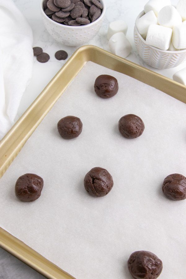 Serve up these easy hot chocolate cookies today. These are a cute and fun chocolate cookie topped with marshmallow and chocolate! Try today. #hotchocolate #cocoacookies #dessert #passion4savings #dessertidea #holiday #christmas #winter #cakemix #devilsfood raw cookie dough balls on baking sheet