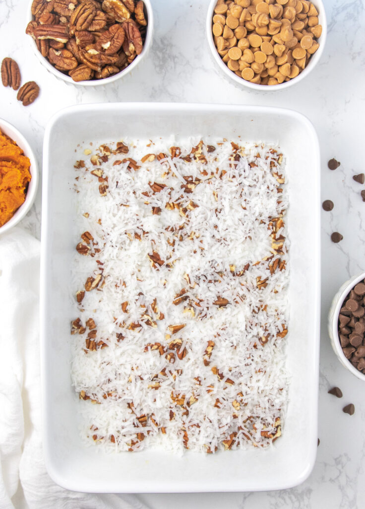 Slice and serve up this incredible pumpkin earthquake cake. A pumpkin cake filled with coconut, pecans, cream cheese swirl and much more. #passion4savings #pumpkin #cake #earthquake #cakemix #fall #dessert #easy #best #holiday #falldessert coconut and pecans in a baking dish