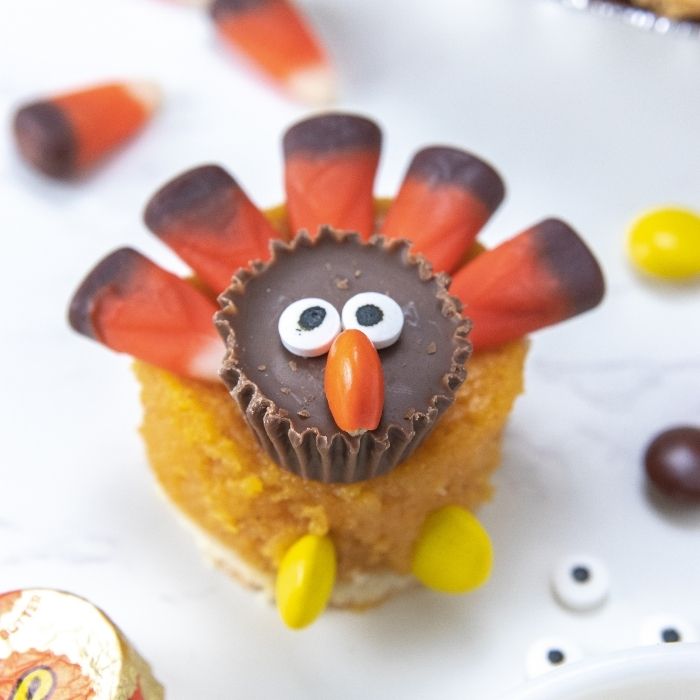 Mini Pumpkin Pie Turkeys are a simple and easy Thanksgiving dessert that are adorable. A round pumpkin pie topped with candies to look like a turkey. A fun and cute Thanksgiving treat for kids and adults. #passion4savings #dessert #thanksgiving #easy #fun #kid #holiday #simple #treatrecipe turkey pumpkin pie dessert on white counter