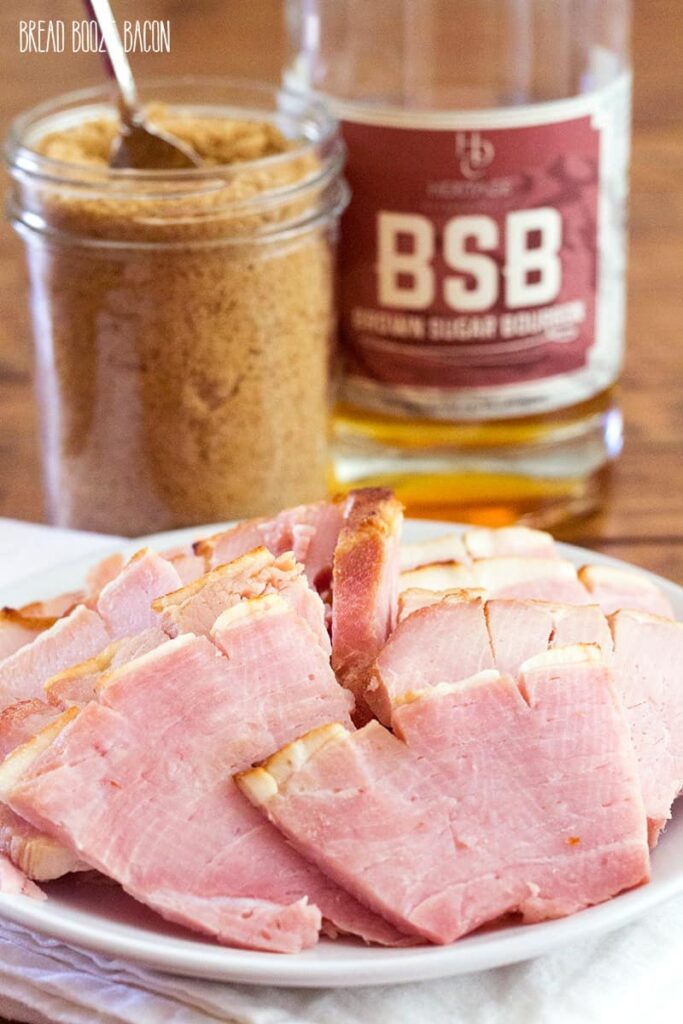 sliced ham on a platter with brown sugar and bourbon in background 
