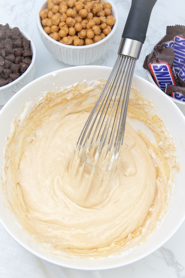 Snicker brownies are a delicious and easy layered brownie. A brownie base, caramel layer, nougat, and chocolate and chopped Snickers! #passion4savings #snickers #brownies #desserttrend #trending #recipe #best #partyfood nougat in a white bowl