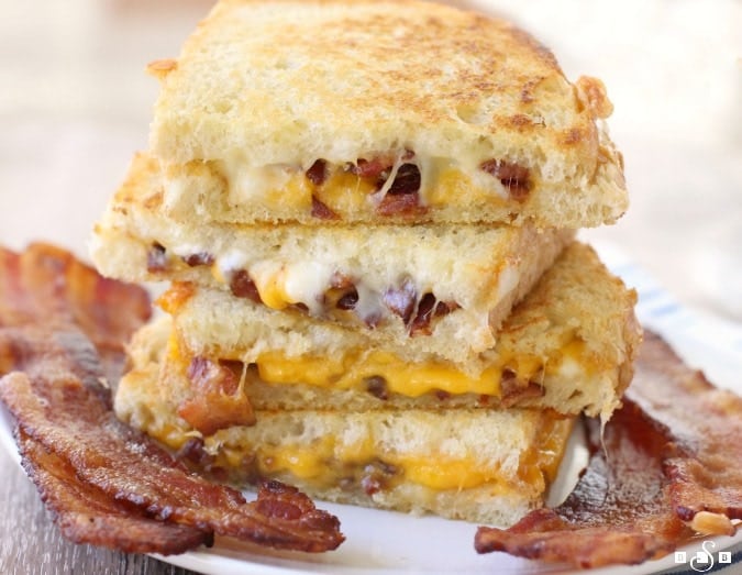stacked grilled cheese on plate with bacon by it 