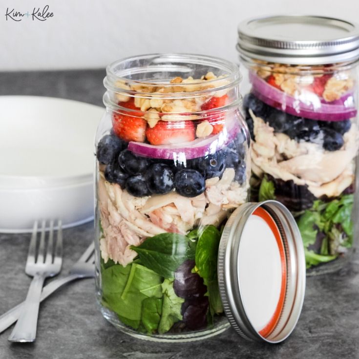 spinach and strawberry salad in jars on the table with fork by it 