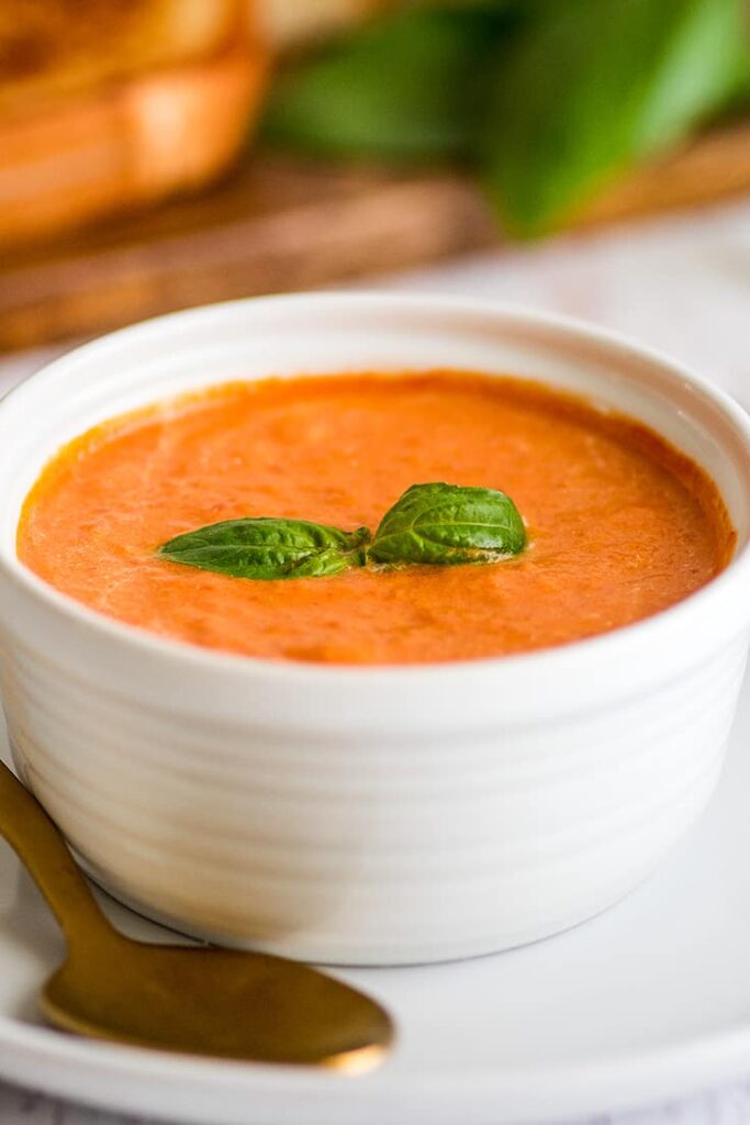 tomato soup in a white bowl with basil leaf in the center 