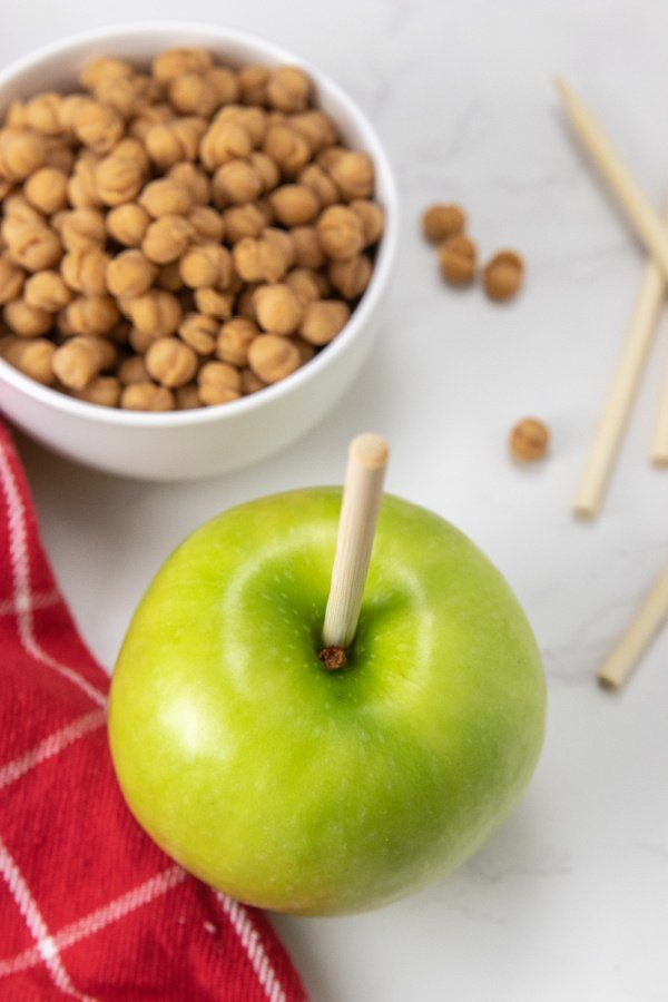 apples with stick in it and caramel bits on counter 