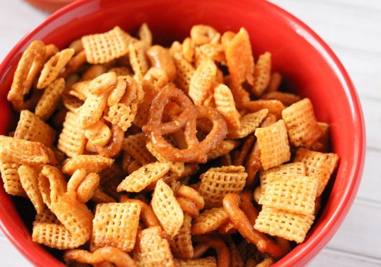 spicy pretzel snack mix in a red bowl on counter 