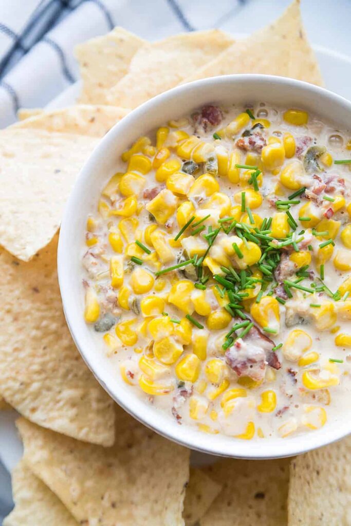 corn dip in a bowl with chips around it 
