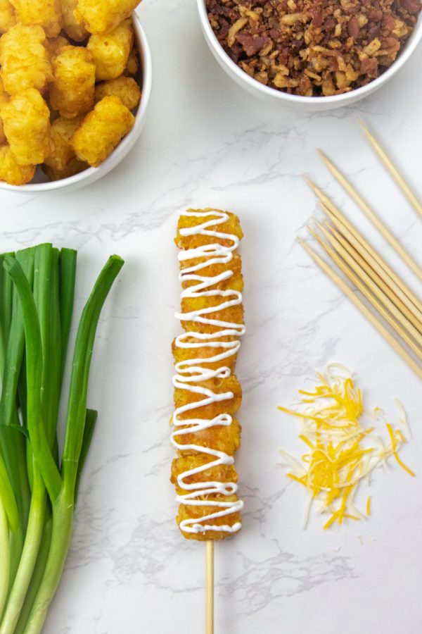 tater tots on skewer with toppings around it on counter 