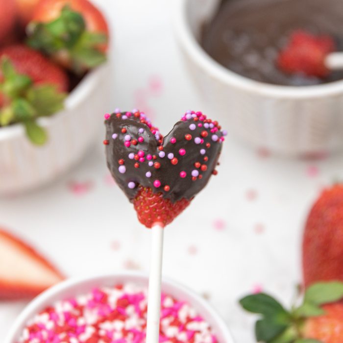 Chocolate Covered Strawberry Heart Pops are a heart shaped strawberry dipped in chocolate and sprinkles on top. A Valentine's Day dessert! #passion4savings #valentinesday #dessert #strawberry #nobake #easy #romantic #quick #dessert #holiday #healthy hearty shaped strawberry dipped in chocolate on a stick