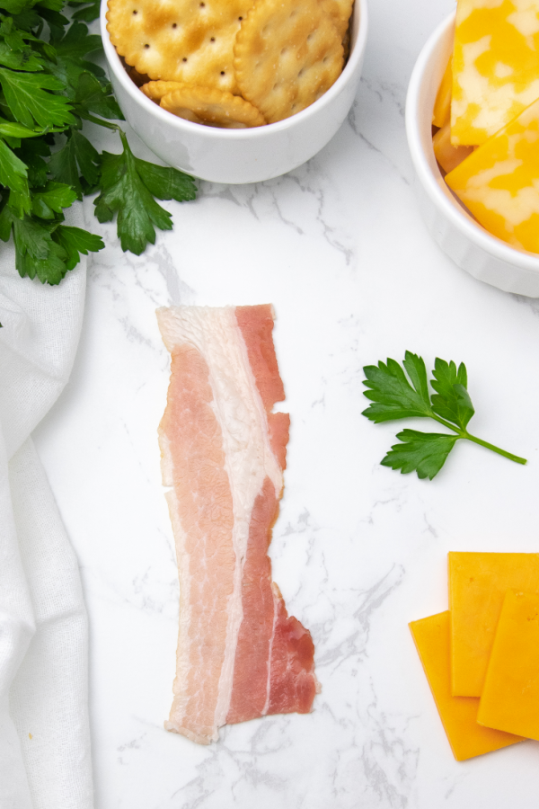 bacon on marble counter with cheese and crackers by it 