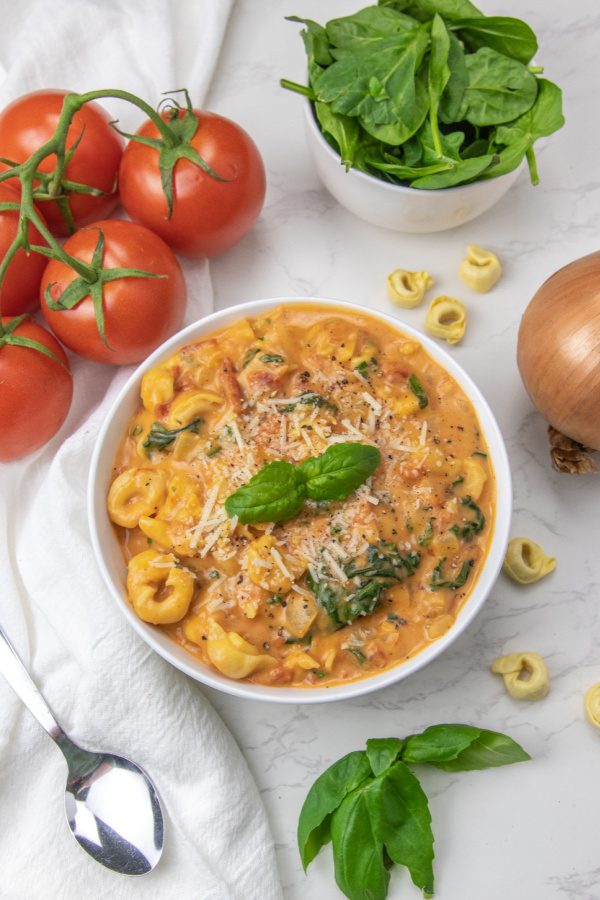 parmesan tortellini soup in a white bowl with ingredients aorund it 